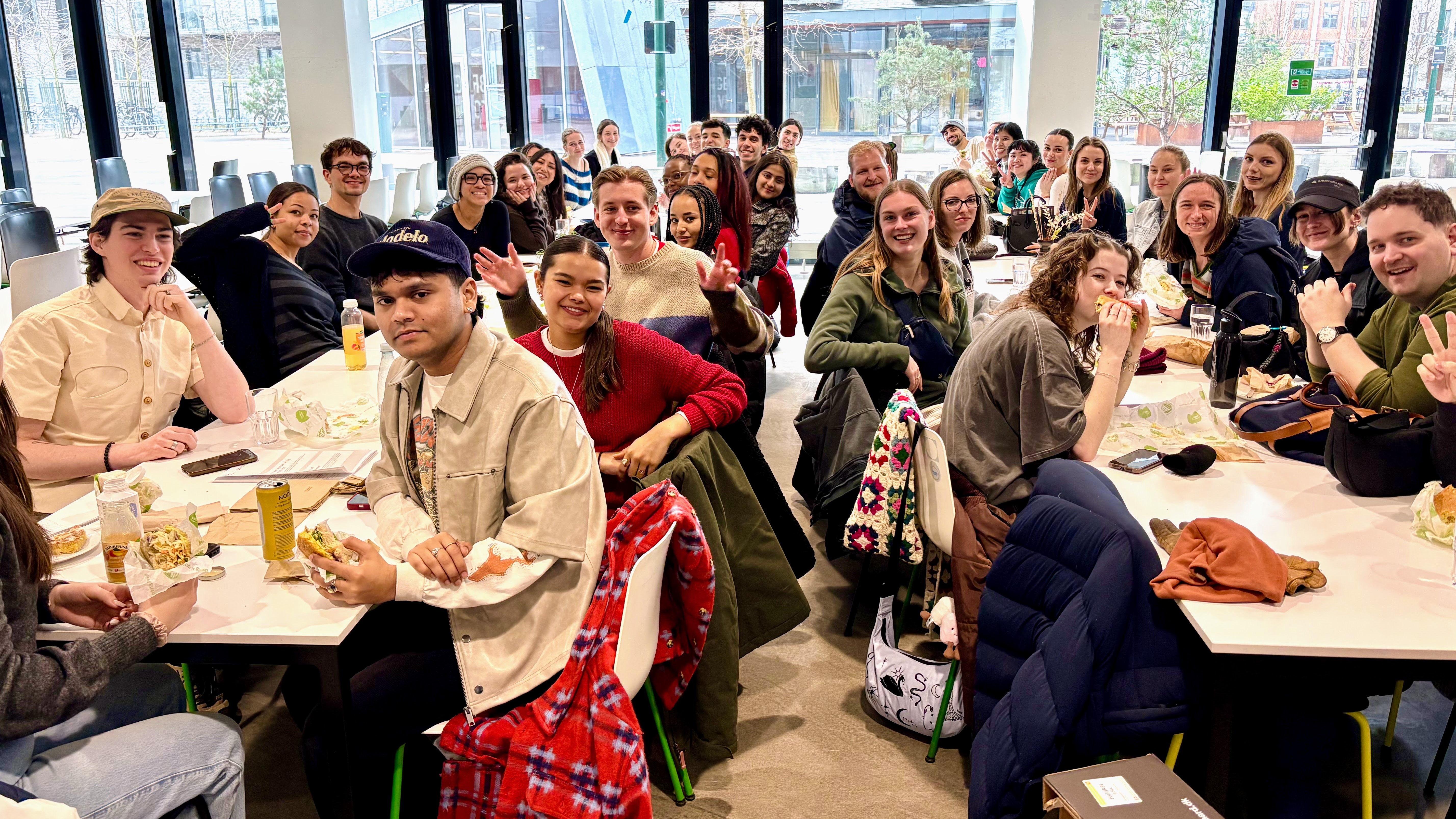 A large group of students sit at two long tables and smile for the camera.