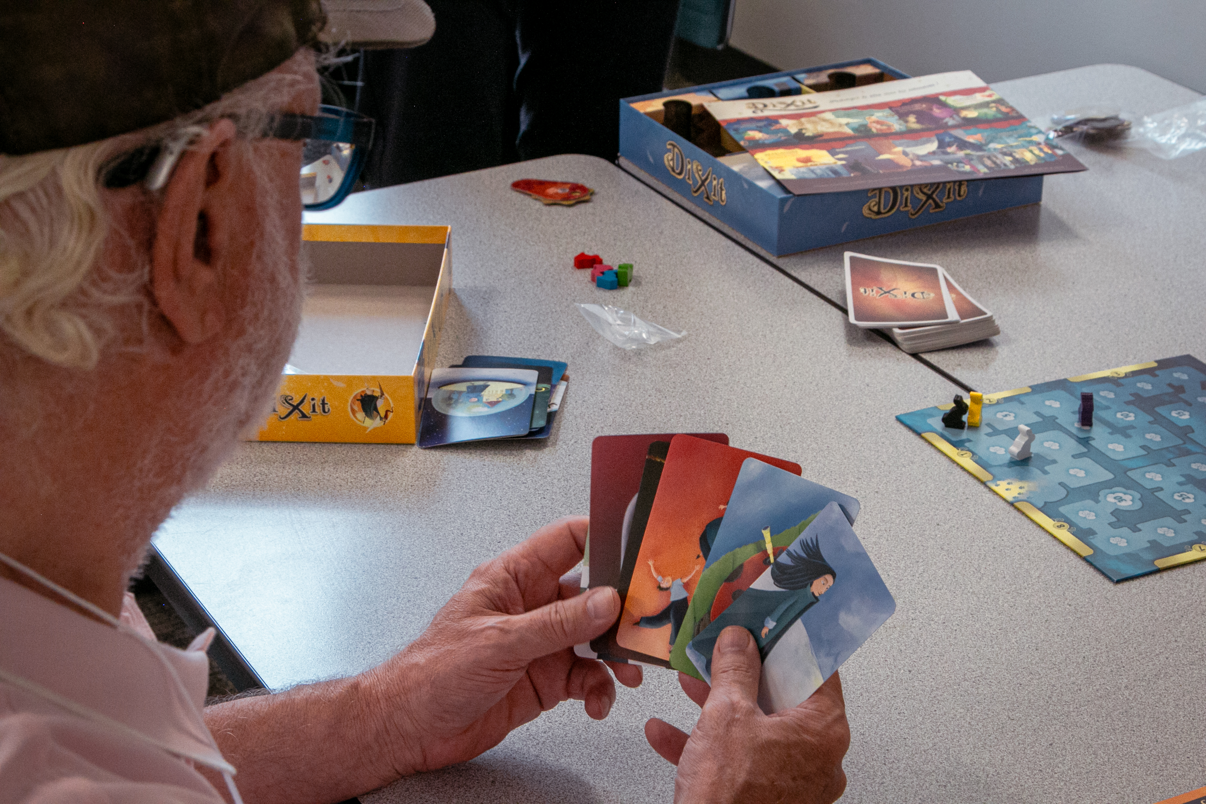 A man holds a hand of cards. The cards show abstract art.