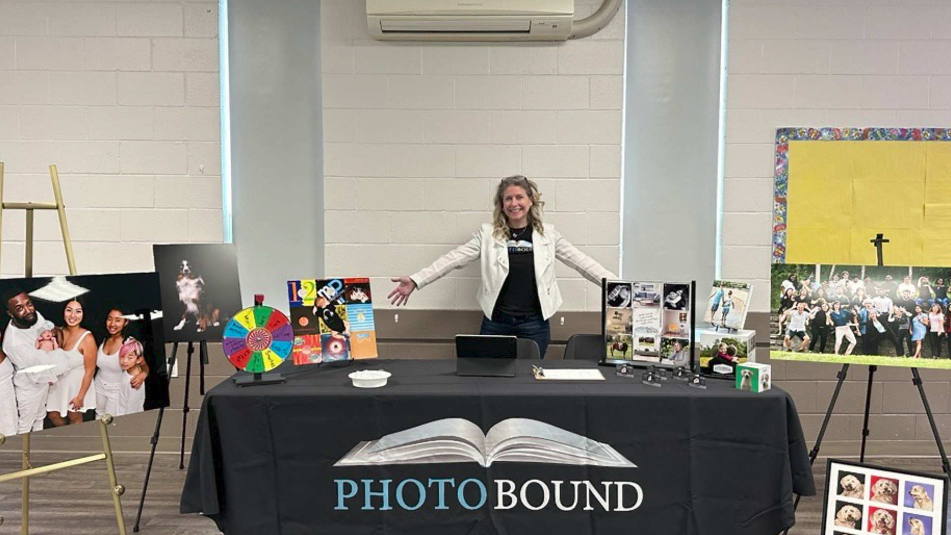 A woman in a white jacket stands behind a table displaying photographs