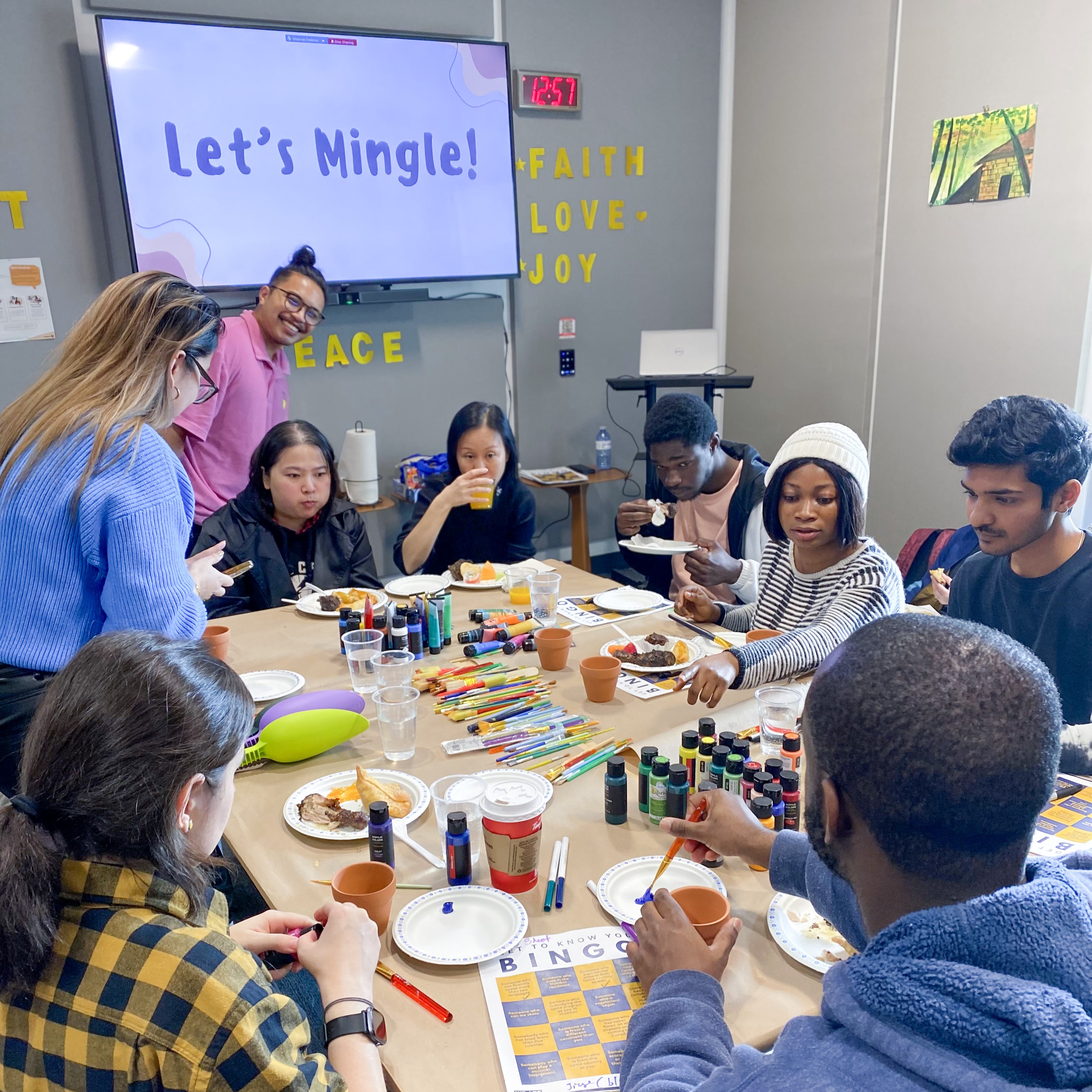 A group of people sit around a table eating snacks and doing crafts.