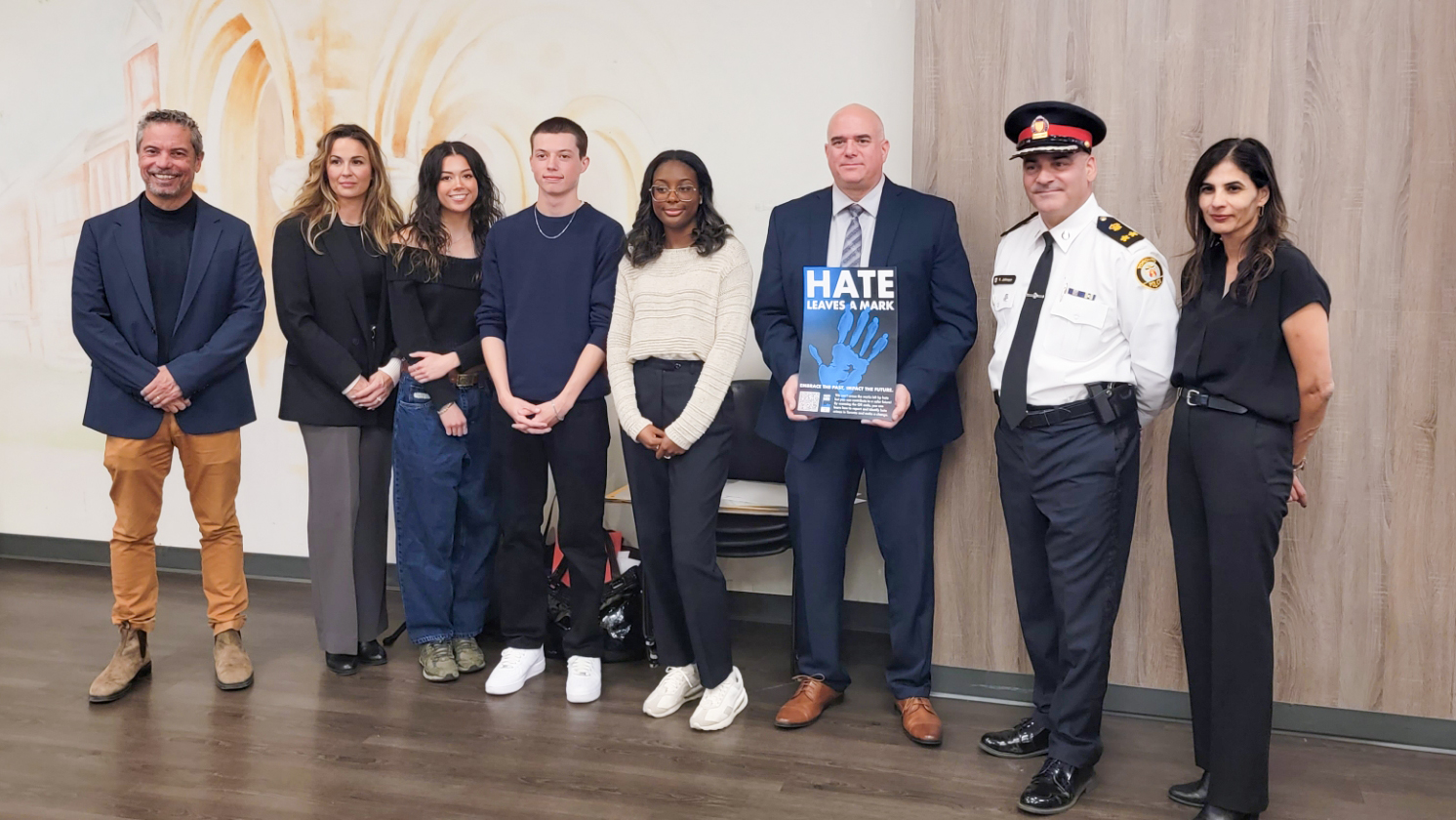 8 people pose together. One person is holding a mock up of a poster that reads "Hate Leaves a Mark"