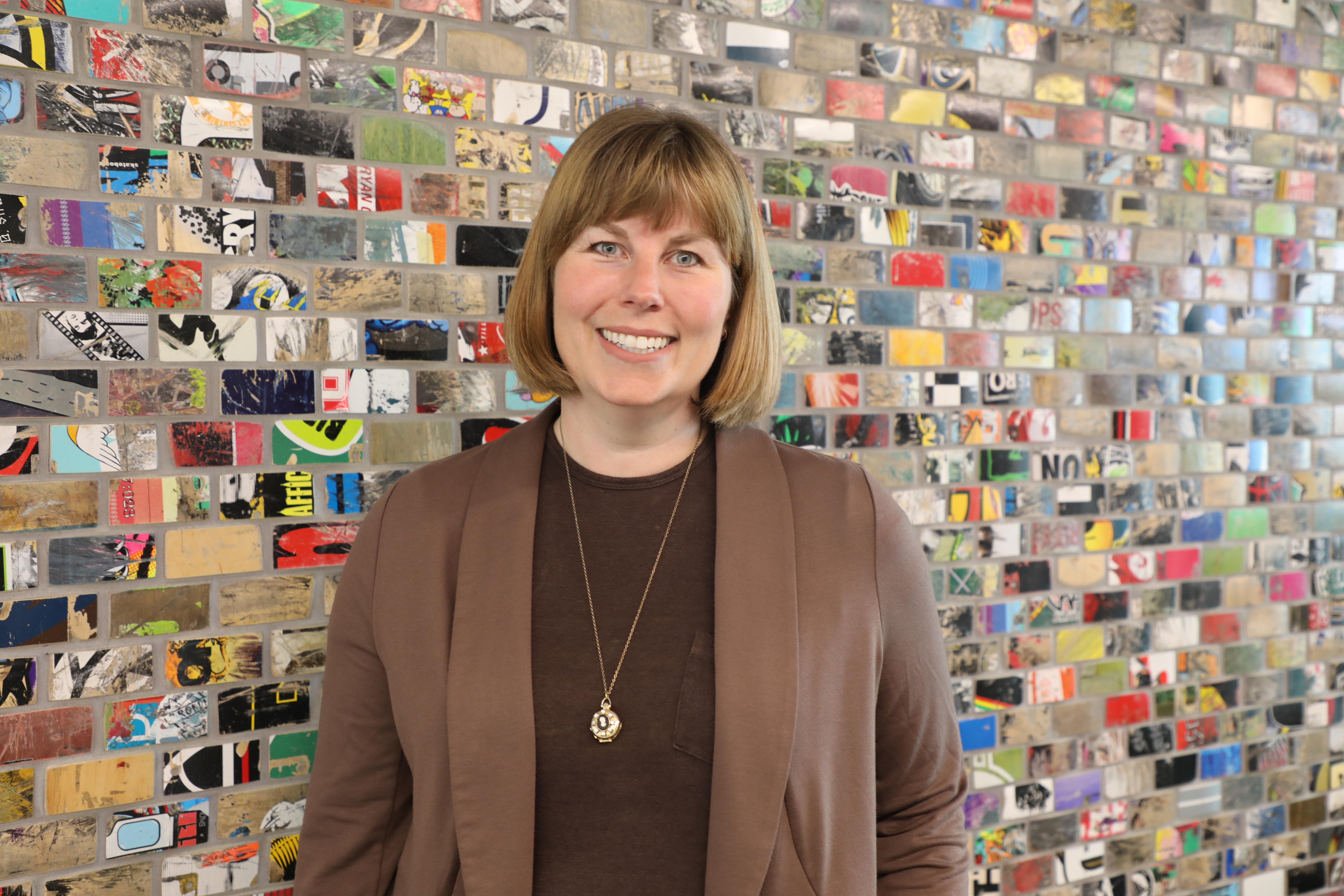 A woman stands in front of a colourful wall.