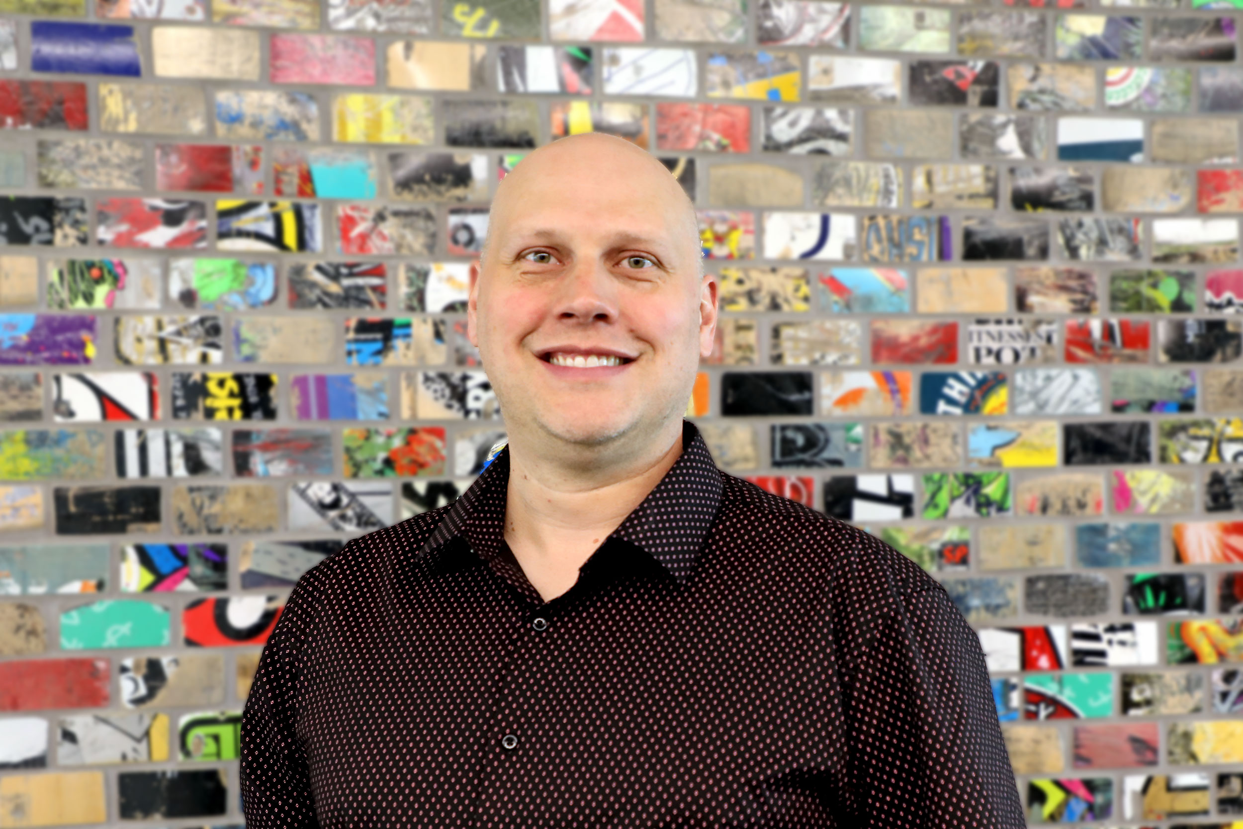 A man stands in front of a colourful wall.