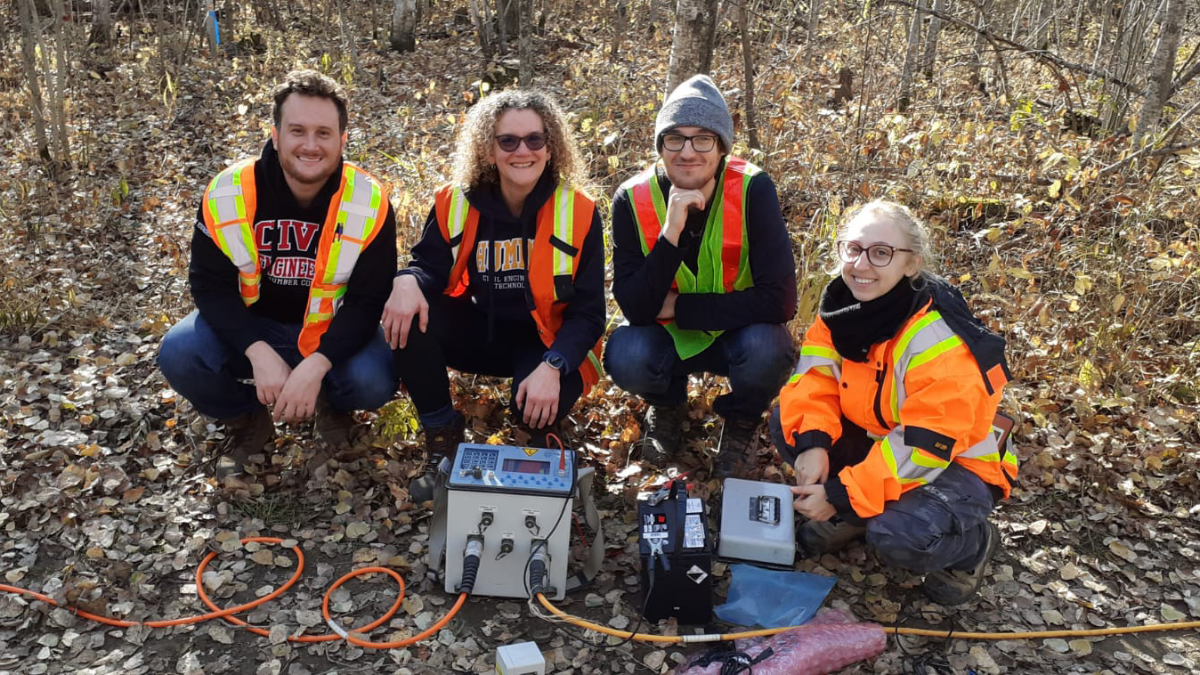 Four researchers crouch on the ground, posing with their geoelectrical equipment